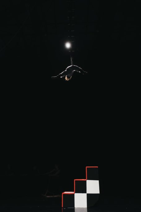 A performer is silhouetted high in the sky above a check board staircase.